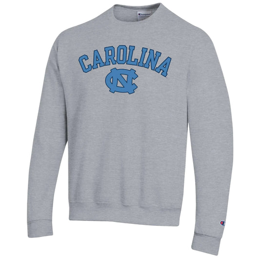 A heather gray crewneck sweatshirt featuring 'CAROLINA' and the NC logo in blue on the chest, with a small Champion logo on the left sleeve cuff.